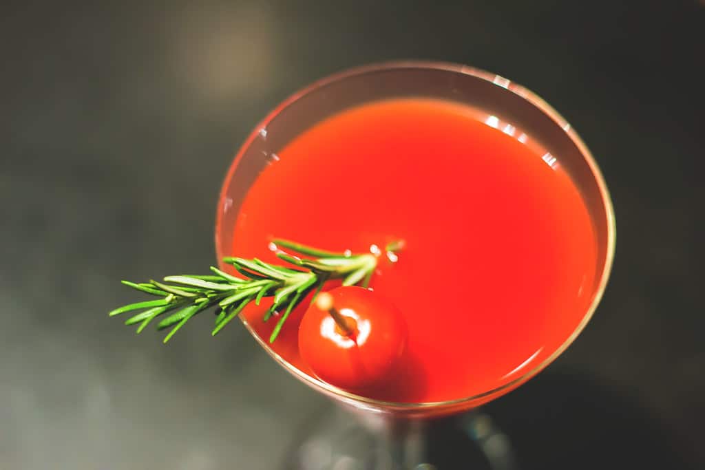 Un verre de bloody mary avec une branche de romarin et une tomate cerise en garnish