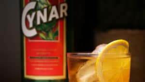 Un spritz de Cynar con una botella de Cynar en fondo